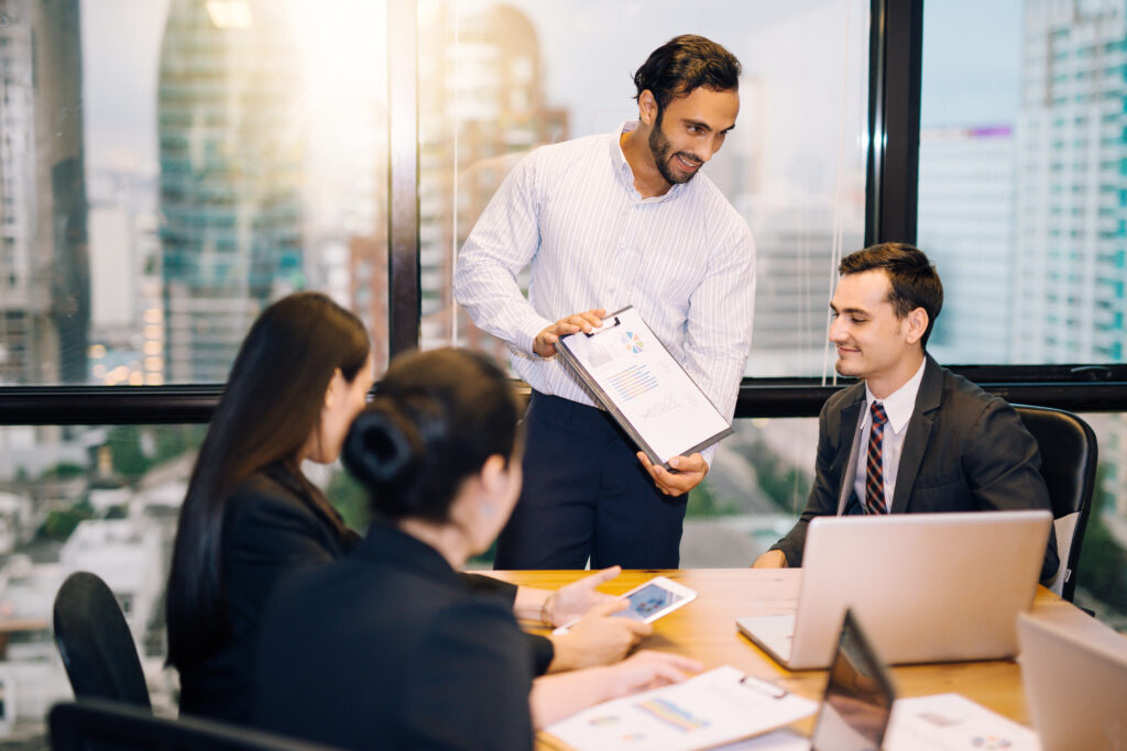 A male sales representative doing a sales pitch in front of his clients.